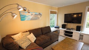 Una sala de estar con un sofá marrón, una mesa de centro, un cuadro en la pared, un televisor y una ventana con persianas.