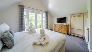 A bedroom with a bed, a TV, a wooden dresser, a radiator, and a window with curtains. - James Ville Marina Lodge 10 (Brigg)