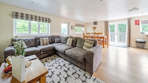A living room with a sectional sofa, a dining table with chairs, a coffee table, and a view of the outdoors through large windows. - James Ville Marina Lodge 10 (Brigg)