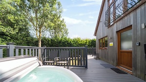 A wooden deck with a hot tub, outdoor seating, and a building with a wooden door and windows. - James Ville Marina Lodge 10 (Brigg)