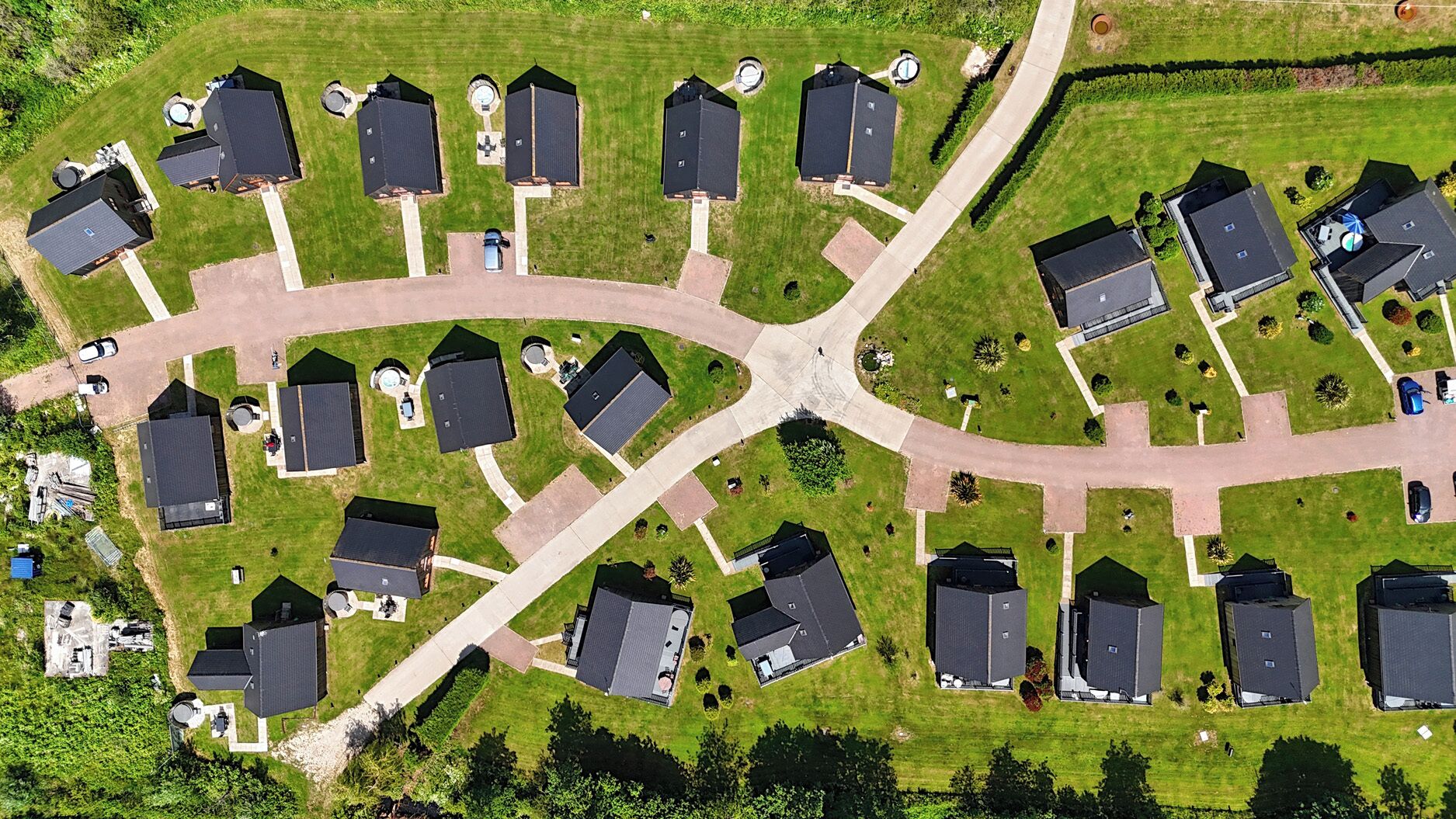 An aerial view of a residential area with multiple houses, a central road, and surrounding greenery.