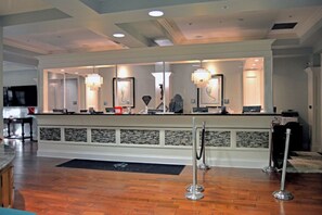 A hotel reception area with a counter, chandeliers, and a black mat on the floor. - Oceanfront Villa | Pool Access | North Myrtle Beach Views (North Myrtle Beach)