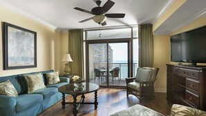 A living room with a blue sofa, a glass coffee table, a television, and a balcony with a view of the ocean. - Oceanfront Villa | Pool Access | North Myrtle Beach Views (North Myrtle Beach)