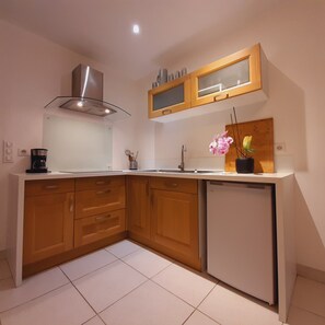 A compact kitchen with wooden cabinets, a stainless steel range hood, a built-in dishwasher, and a small refrigerator. - Gîte des Remparts - Charming apartment in the heart of Lucéram with mountain view (Lucéram)