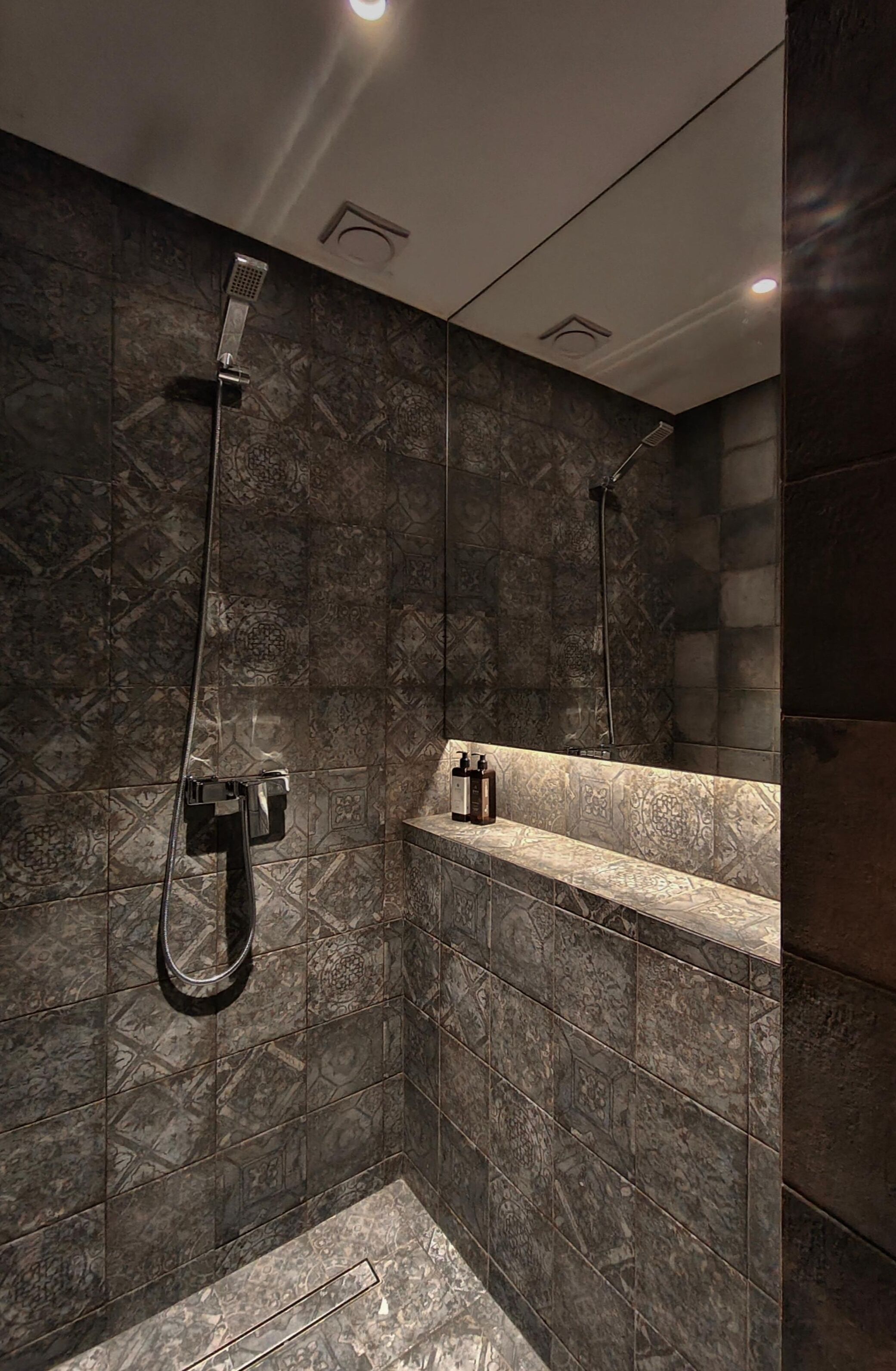 A modern bathroom with a shower, a built-in bench, and patterned tiles.