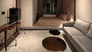 A modern hotel room with a bed, a sofa, a TV on a stand, and a small round table. - ModernInfluence (Porto)