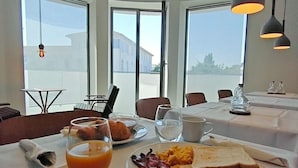 A breakfast setting with a table, breakfast items, and large windows. - ModernInfluence (Porto)