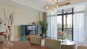 A modern living room with a wooden dining table, comfortable seating, a television, and a large window with curtains. - Vesta - Luxury Apt - 2BR - CFC (XVI) (New Cairo City)