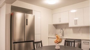 A modern kitchen with white cabinetry, a stainless steel refrigerator, a marble countertop, and a dining table with chairs. - 4615 Inverness Street Vancouver King And Queen 2 Bedrooms Suite Private Entry (Vancouver)