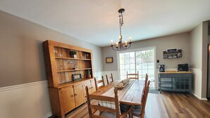 Een eetgedeelte met een houten tafel en stoelen, een houten kast met planken, een kroonluchter en een koffiehoek.