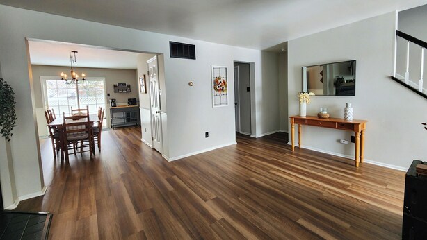 Een ruime woonkamer met houten vloeren, een eettafel en een houten console met decoratieve objecten.