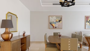 A dining area with a wooden table, cushioned chairs, a lamp, and artwork on the walls. - Vesta - Luxury Apt - 2Br - Cfc (XXXI) (New Cairo City)