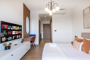 A modern hotel room with a large bed, a desk with a chair, a television displaying Netflix content, and an air conditioning unit. - Luxury suite in Downtown Punta Cana (Punta Cana)