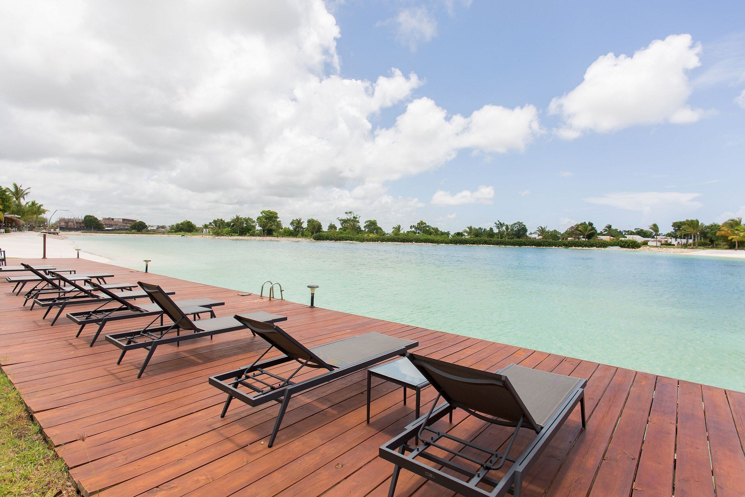 A wooden deck with sun loungers overlooking a clear turquoise sea.