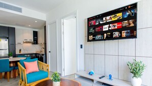Een moderne woonkamer met een houten salontafel, een blauwe bank en een aan de muur bevestigde televisie met verschillende programma's.