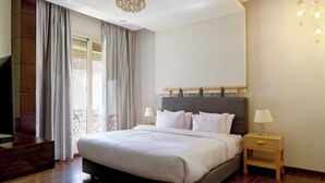Ein modernes Schlafzimmer mit einem großen Bett, Holzboden, einem Fernseher und einem Balkon mit Vorhängen.