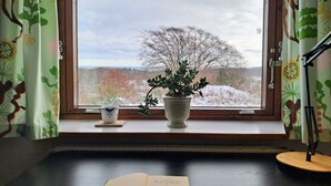 Et værelse med et vindue, en potteplante, en kop og en åben bog på et bord.