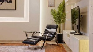 Een moderne woonkamer met een leren fauteuil, een potplant, een flatscreen televisie en een minimalistisch design.