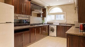 Een moderne keuken met donkere houten kastjes, roestvrijstalen apparatuur, een inbouwoven, magnetron en vaatwasser.