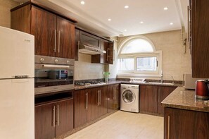 A modern kitchen with dark wood cabinets, stainless steel appliances, a built-in oven, microwave, and dishwasher. - VESTA - Luxury APT - 3BR - New Cairo (I) (New Cairo City)