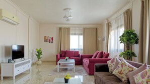 A living room with a flat-screen TV, a white coffee table, a red sofa, and a brown sofa with floral cushions.