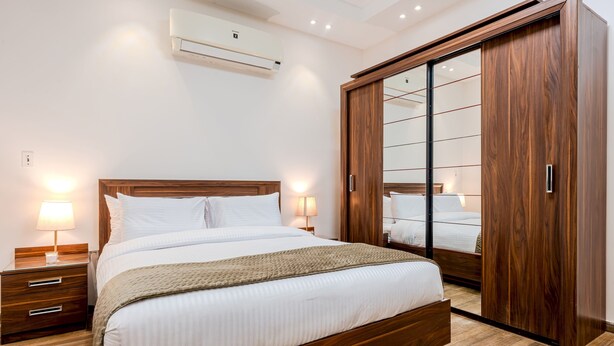 Un dormitorio ordenado con una cama de madera, mesitas de noche, un armario con puertas de cristal y un equipo de aire acondicionado.