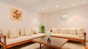 Un salon moderne avec deux canapés beige, une table basse en verre, un vase décoratif et une œuvre d’art murale.