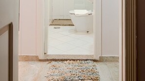 Un couloir étroit mène à une salle de bain équipée de toilettes, d’un lavabo et d’une zone douche.