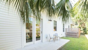 Een wit huis met een overdekte patio, een kleine tafel met stoelen en een palmboom.