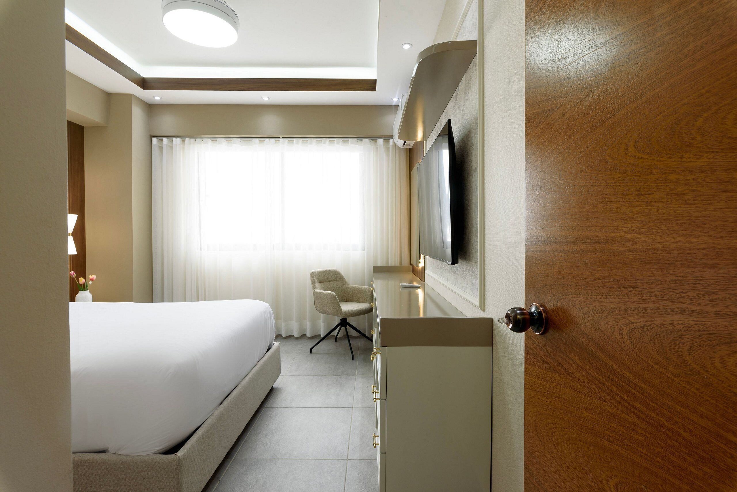 Una habitación de hotel con cama, escritorio, silla y televisión montada en la pared.