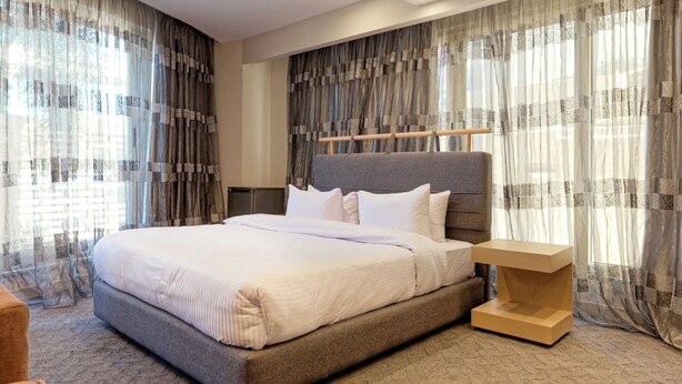 A modern bedroom with a large bed, a bedside table, and sheer curtains. - VESTA - Luxury Studio - New Cairo (I) (New Cairo City)