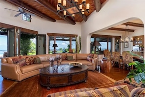A spacious living area with a large sofa, a round coffee table, and a dining area with chairs. - Spanish Mansion - Architectural Delight! (Perris)