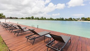 A wooden deck with sun loungers overlooking a clear turquoise sea.