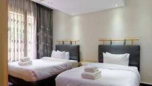 Habitación de hotel con dos camas, cada una con cabecera gris y ropa de cama blanca.