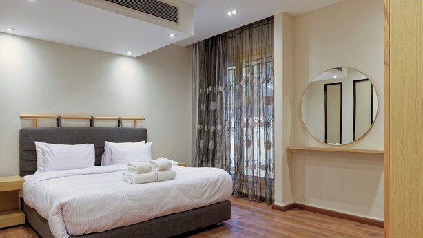 Una habitación de hotel moderna con una cama grande, un espejo redondo y suelo de madera.