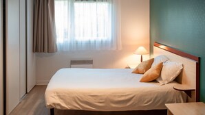 A hotel room with a bed, a bedside table, a lamp, and a window with curtains.