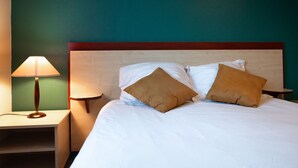 Cama bem arrumada com lençóis brancos e duas almofadas marrons, luminária de cabeceira e mesa de cabeceira de madeira.