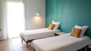 A hotel room with two single beds, a teal accent wall, a white curtain, and a bedside lamp. - Charmant studio au Cœur de Brest | Près de la Mer (Brest)
