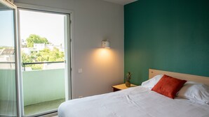 Een hotelkamer met een bed, een nachtkastje, een wandlamp en uitzicht op het balkon.