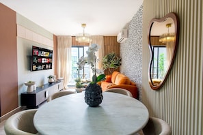 Ein modernes Wohnzimmer mit einem runden Esstisch, einer Wand-TV und einem Sofasofa, sowie einem spiegel mit Herzform.