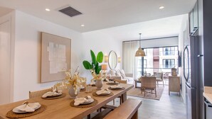 Un espace repas moderne avec une table en bois dressée pour quatre personnes, un banc et une vue sur le salon.