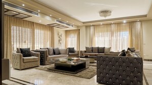 A spacious living room with a large sectional sofa, a tufted armchair, and a coffee table. - VESTA - Luxury Villa - 6BR - New Cairo (New Cairo City)