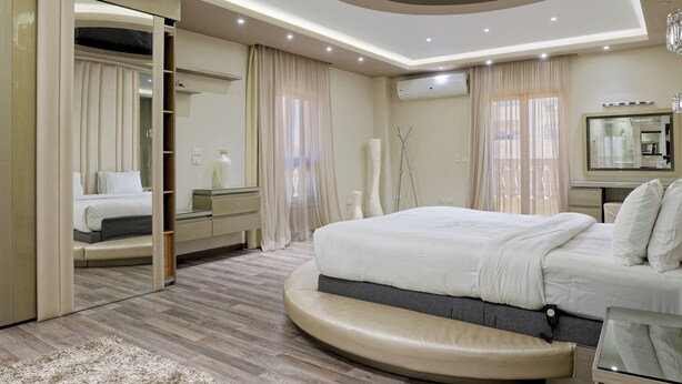 A modern bedroom with a large bed, a built-in wardrobe, and a round seating area. - VESTA - Luxury Villa - 6BR - New Cairo (New Cairo City)