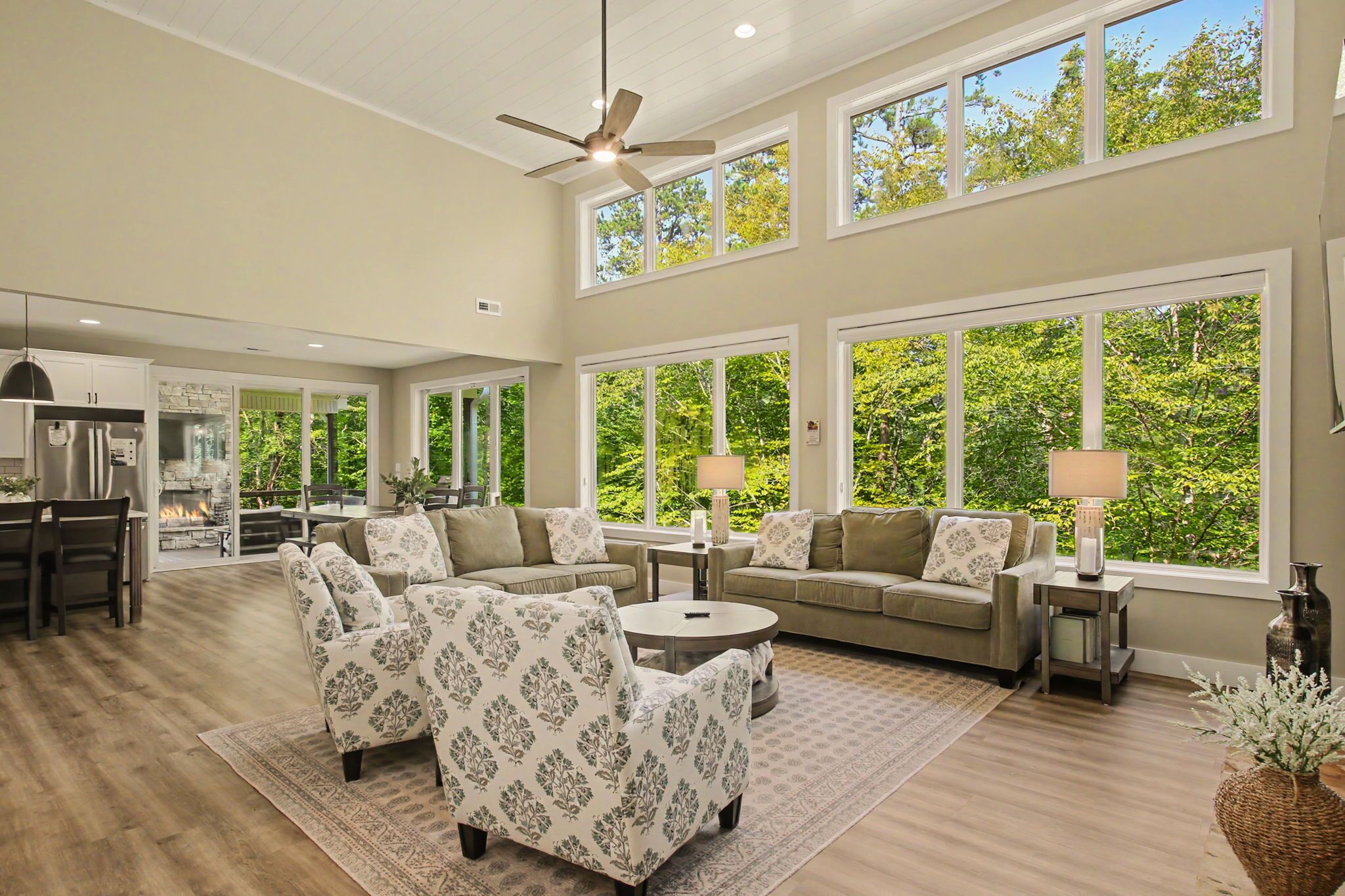 A spacious living room with a high ceiling, large windows, and a fireplace.