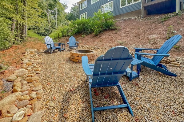 A backyard with a fire pit, Adirondack chairs, and a stone wall.