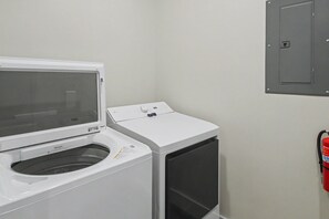 A laundry room with a front-loading washer and dryer, a fire extinguisher mounted on the wall, and a utility panel above the dryer.
