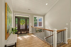 A staircase with a wooden handrail and black balusters, leading to a door with a glass panel. - New Lakefront Estate | Sleeps 34 | Private Dock (LaFollette)