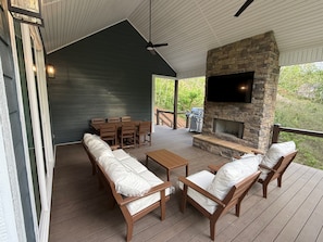 Un patio techado al aire libre con chimenea de piedra, muebles de madera y un televisor montado en la pared.