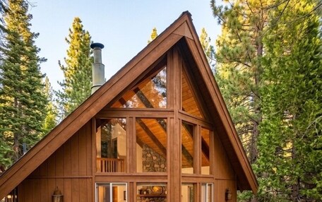 A wooden cabin with a deck, a fireplace, and a stone wall.