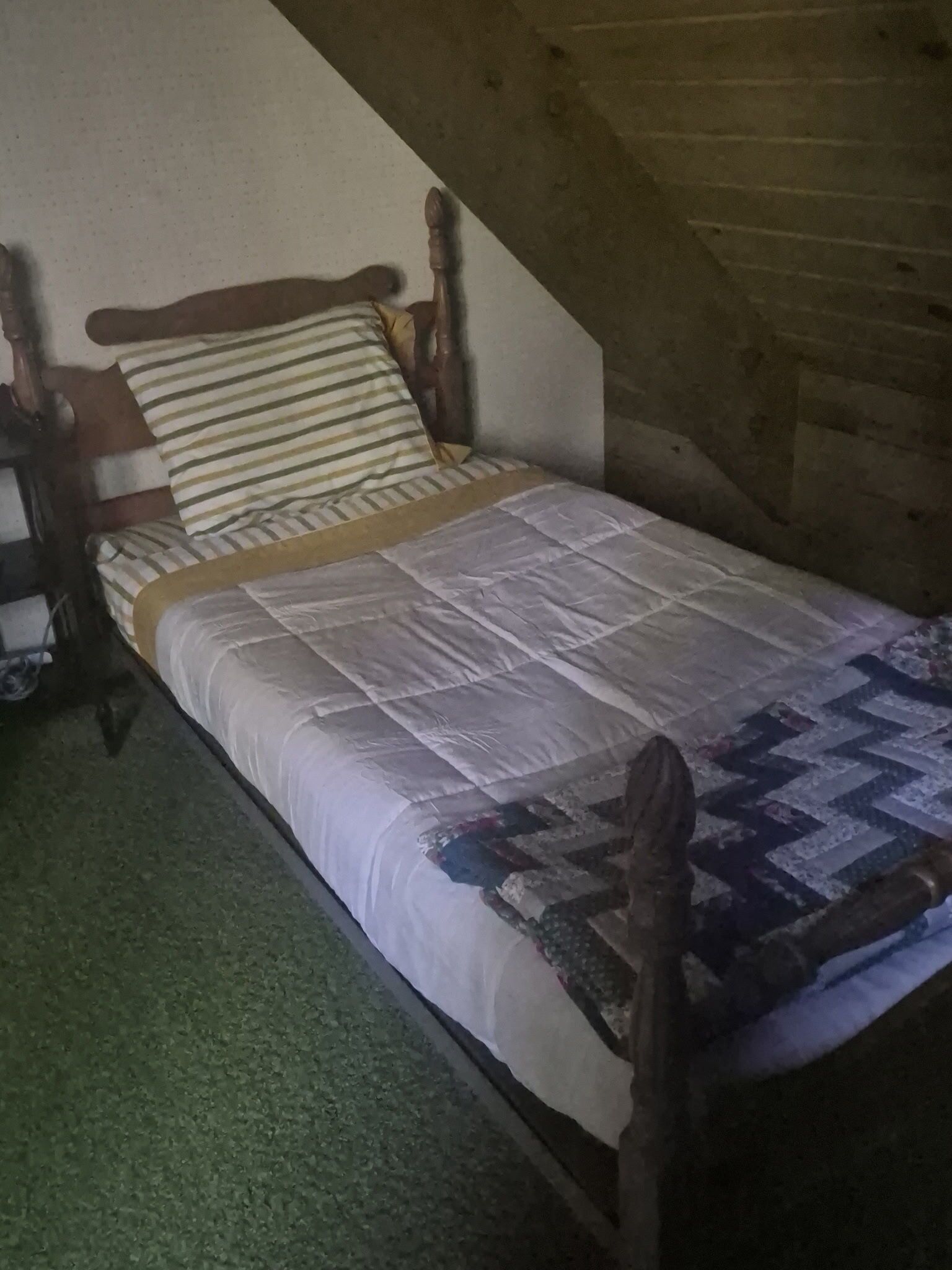 Uma cama de solteiro com estrutura de madeira, almofada listrada e colcha.